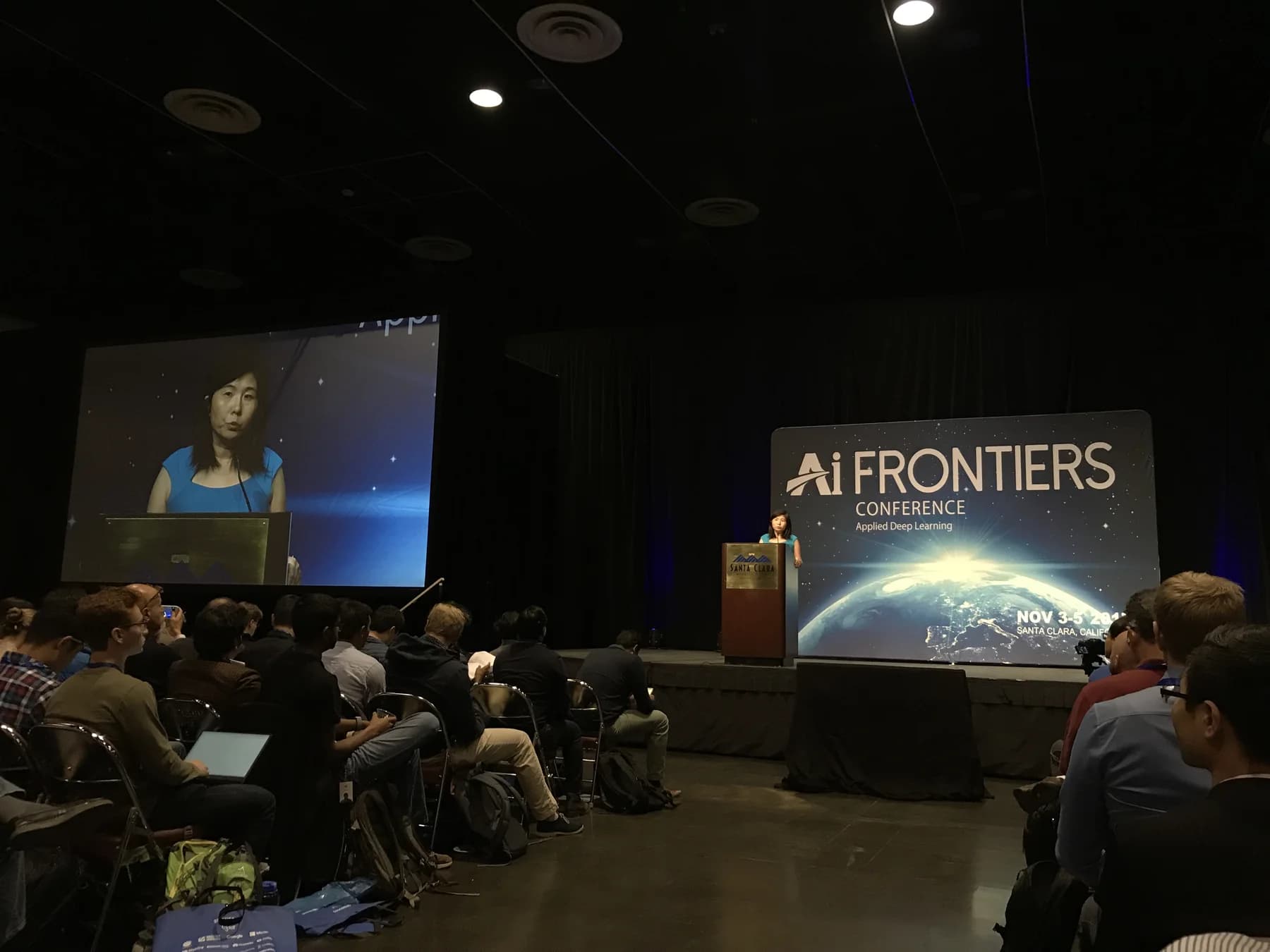 A speaker on stage at AI Frontiers 2017 in Santa Clara, with the event backdrop and audience visible.