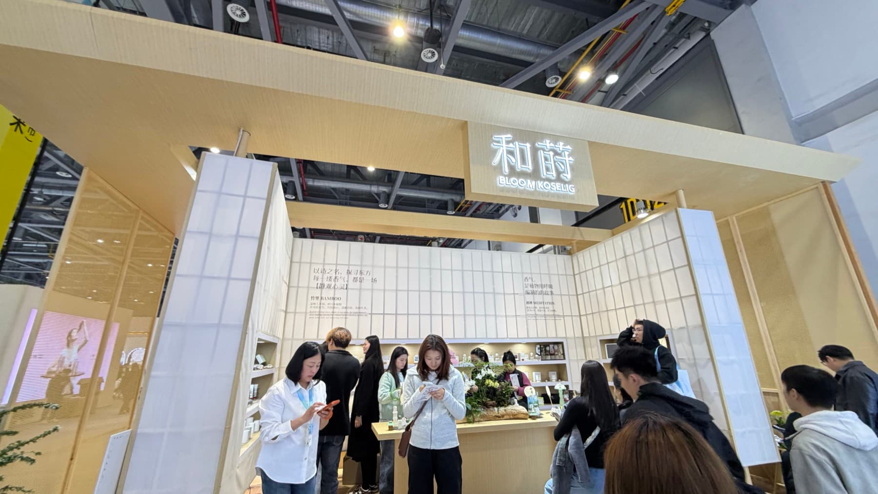A Bloom Koselig booth at CiE 2026 with light wood framing, product shelves, and visitors.