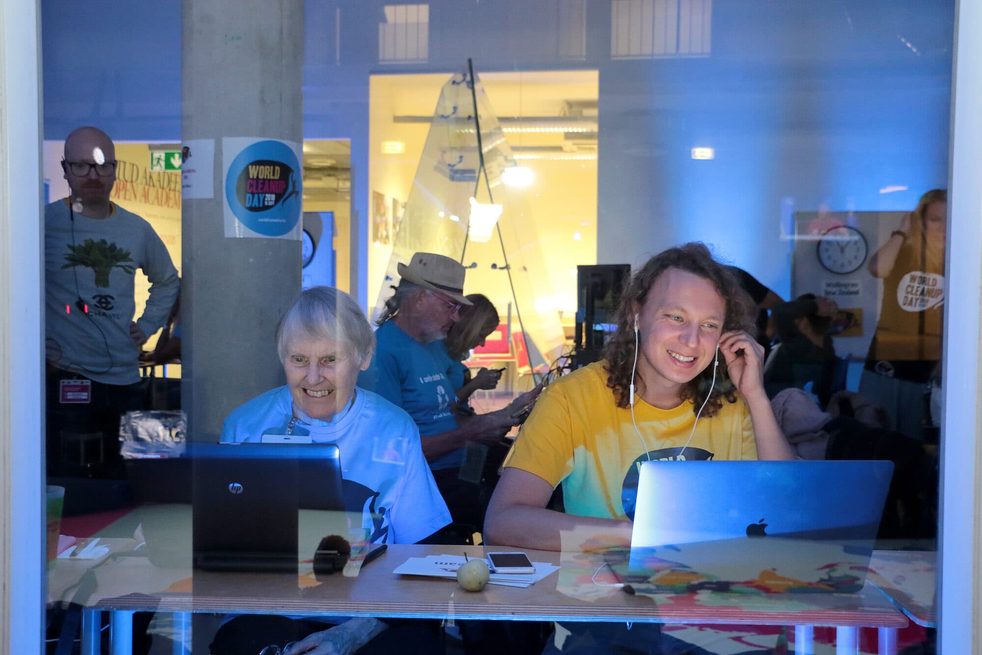 Volunteers working on laptops behind a window in Tallinn during World Cleanup Day 2018, with World Cleanup Day stickers on the glass and wall.
